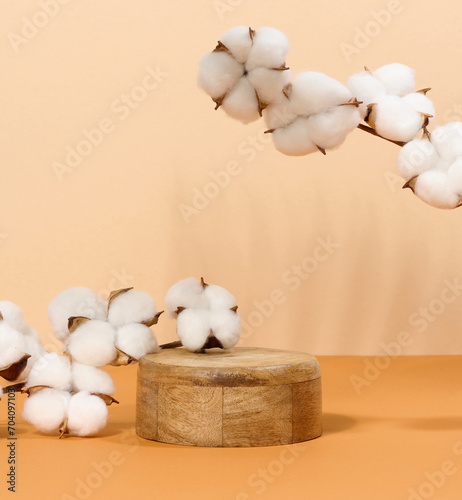 Fototapeta Naklejka Na Ścianę i Meble -  Round wooden platform and cotton branch with white flowers on beige background