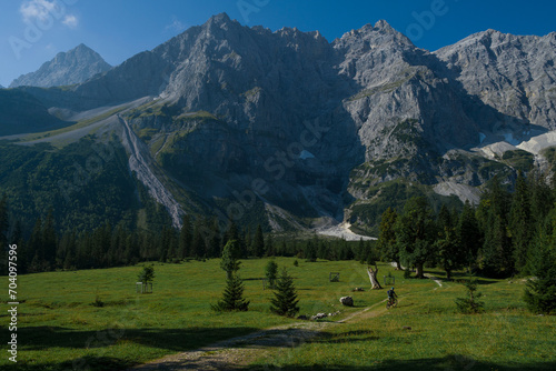 Mountainbiking through Kleiner Ahornboden in the Karwendel mountains in front of steep cliffs during sunny blue sky day in summer, Tyrol Austria.