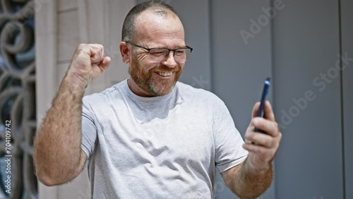 Eureka! cheerful middle-aged caucasian man with beard, firstly celebrating using smartphone on outdoor city street, texting a winning message! photo