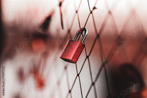 A red padlock hanging on a bridge fence as a sign of love and romance.