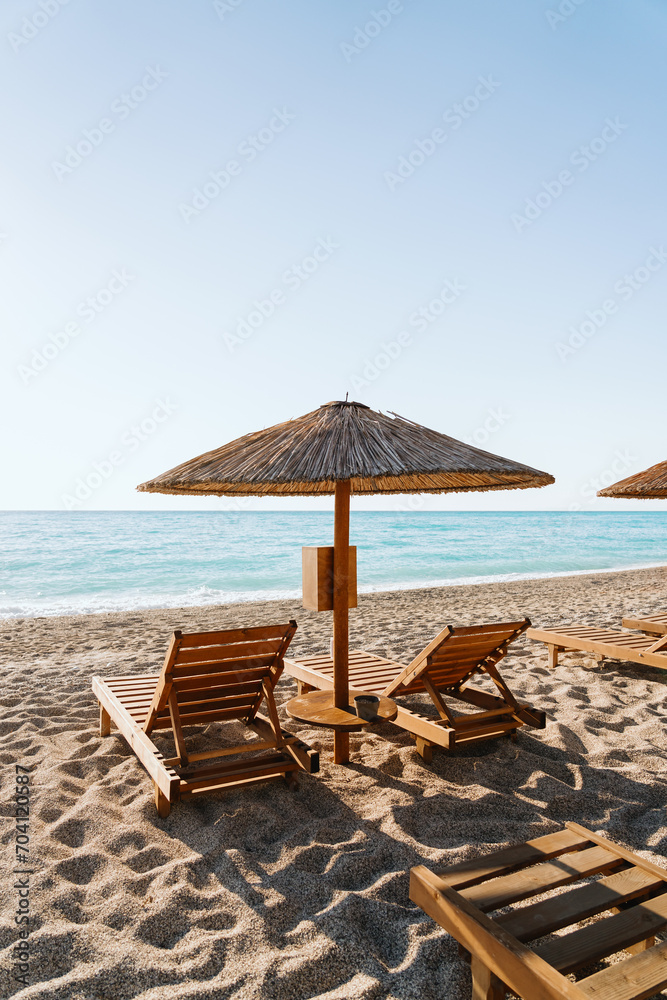 Wooden loungers await under rustic straw umbrellas on a sun-kissed beach, relaxation by the turquoise sea Wooden loungers await under rustic straw umbrellas on a sun-kissed beach, relaxation by the turquoise sea