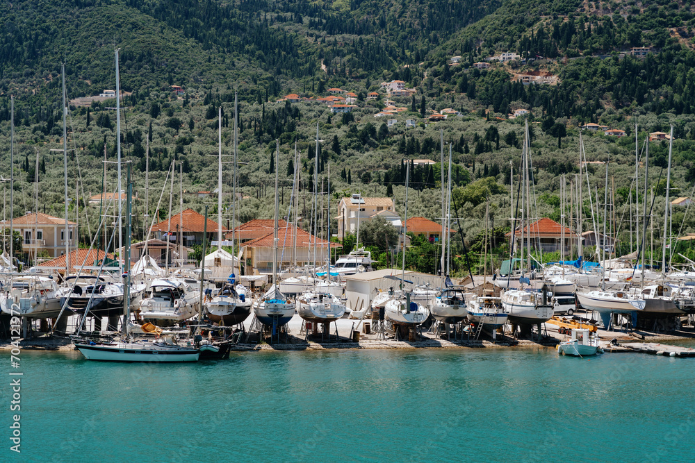 Yachts and sailboats docked at a marina, nestled in a lush, mountainous coastline, under the Mediterranean sun