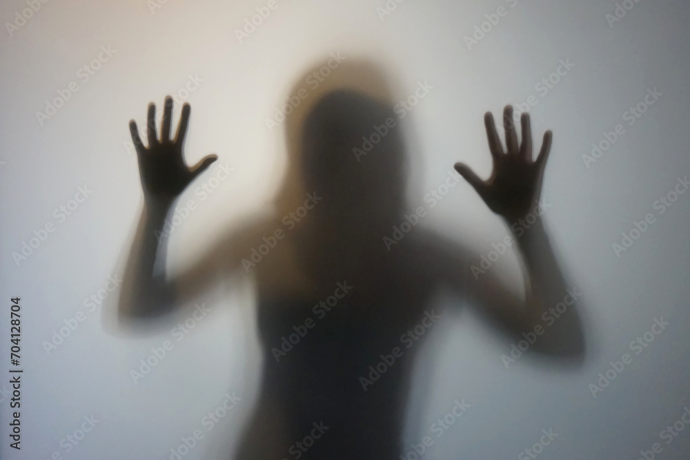 Woman silhouette with raised hands behind frosted glass