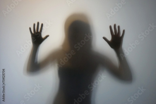 Woman silhouette with raised hands behind frosted glass