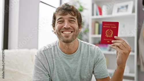 Happy young man elated on his couch, confidently holding his italian passport, ready for a vacation adventure from the comfort of his home! photo