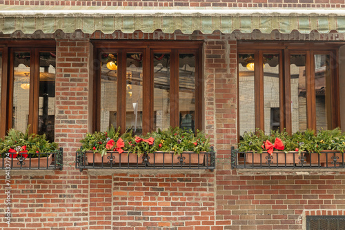 A beautifully decorated storefont with windows under a banner with rustic, beautiful brick in the North End of Boston. This restaurant outdoor space has holiday flowers and even afternoon lighting. photo