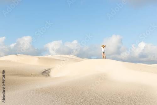 Fototapeta Naklejka Na Ścianę i Meble -  woman on sand dunes faced away wearing denim shorts and a hat 