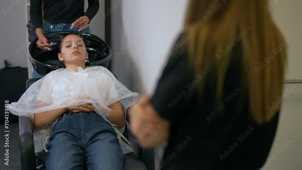 A woman hairdresser talks about the benefits of hair care products while a female client lies in a chair with balm on her hair A woman hairdresser talks about the benefits of hair care products while a female client lies in a chair with balm on her hair