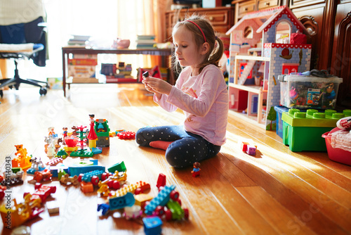 Adorable preschooler girl sitting on the floor and playing with colorful construction blocks