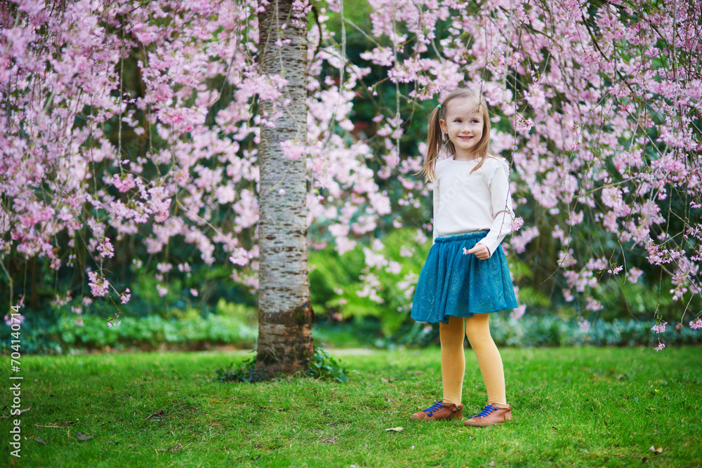 Adorable preschooler girl enjoying nice spring day in park during cherry blossom season Adorable preschooler girl enjoying nice spring day in park during cherry blossom season
