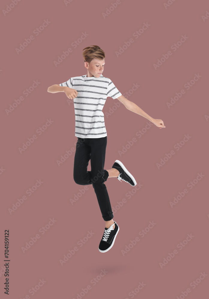 Teenage boy jumping on dusty pink background, full length portrait