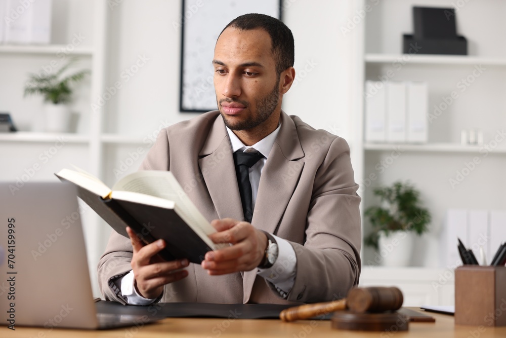 Serious lawyer reading book at table in office