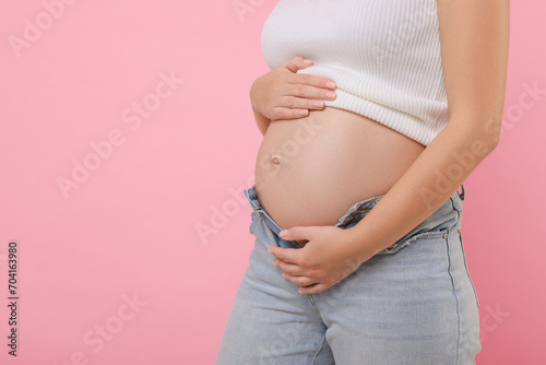 Pregnant woman in jeans on pink background, closeup. Space for text © New Africa