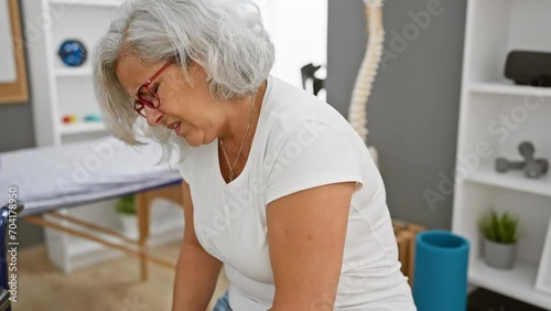 Mature woman with grey hair feeling knee pain at the rehab clinic. photo