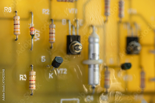 Electronic circuit board made of yellow fiberglass with soldered resistors and capacitors on metal legs marked with letters and numbers. Computer circuit close-up in blur with copy space.