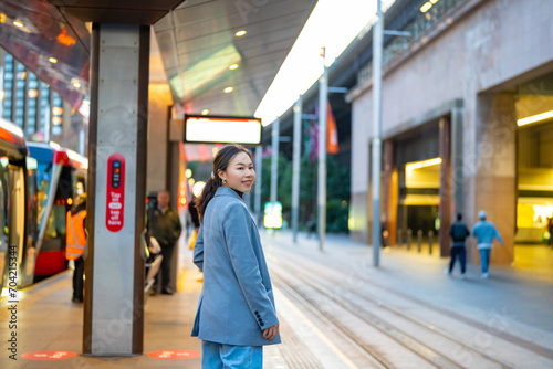 Asian woman waiting for tram at station in the city. Attractive girl tourist enjoy urban outdoor lifestyle travel city street by public transportation on holiday vacation.