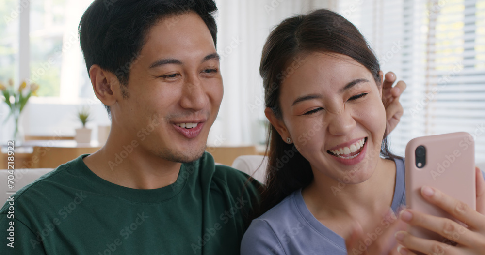 Fototapeta premium Asia people young couple relax leisure good easy time at cozy sofa home enjoy fun play phone trending filter effect selfie challenge in social media app IG reel tiktok viral video story photo shoot.
