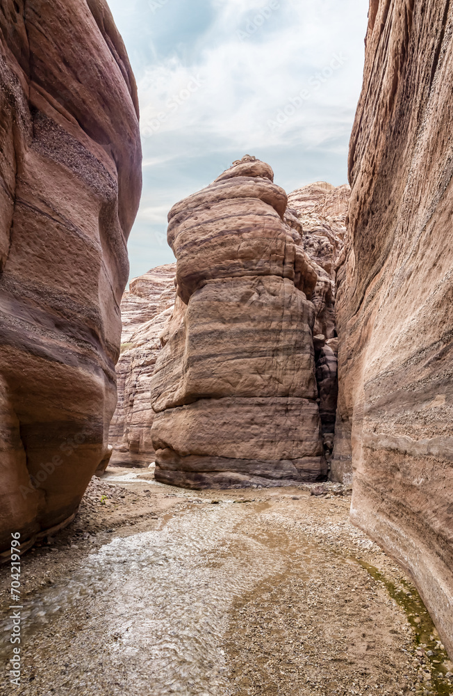 A small  shallow stream flows between high rocks with beautiful natural patterns on their walls at end of a hiking trail in the Wadi Numeira gorge in Jordan