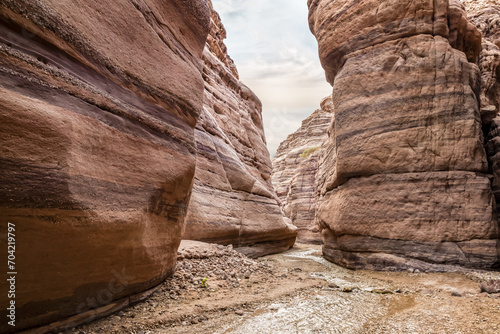 A small  shallow stream flows between high rocks with beautiful natural patterns on their walls at end of hiking trail in the Wadi Numeira gorge in Jordan photo