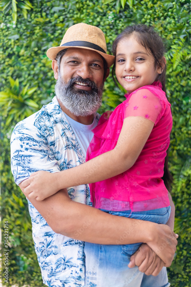 Fototapeta premium Senior looking Indian father wearing hat holding daughter and enjoying in shopping mall.