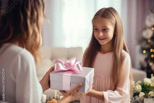 blond girl with slanted eyes gives a box with a gift to her mother in a bright living room. Gift exchange concept, new year, mother's day, birthday.