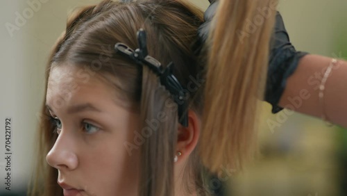 Close-up of a girl head with hairclips in her hair. A hand in a black rubber glove removes the hairclip and untwists the strand of hair, that was held in place by the hairclip. photo