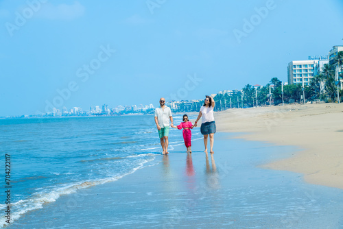 Happy indian Family of three walking on tropical beach and enjoying summer vacation. father and mother holding hands of their daughter. friendly family Concept.
