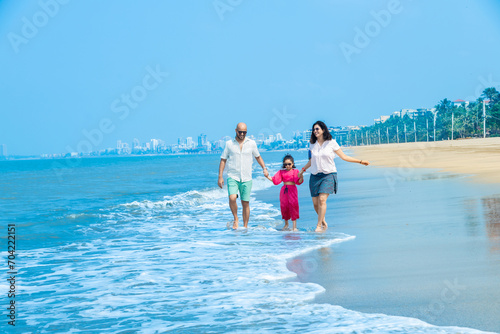 Happy indian Family of three enjoying summer vacation on tropical beach. father and mother holding hands of their daughter. friendly family Concept. photo