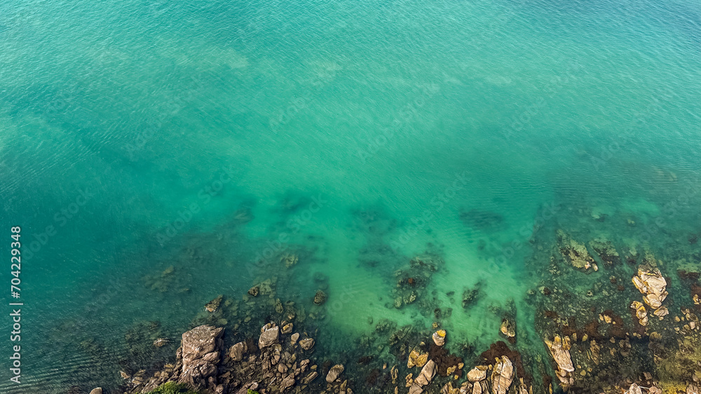 Aerial view of a tranquil, clear turquoise sea gently lapping over a rocky shore, ideal for nature or travel-themed designs