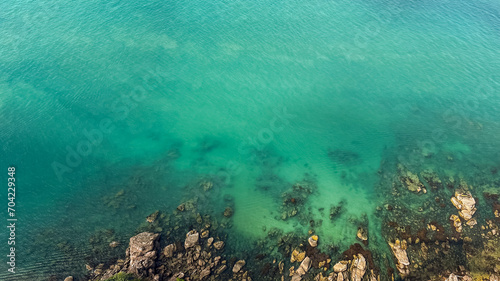 Photography Aerial view of a tranquil, clear turquoise sea gently lapping over a rocky shore