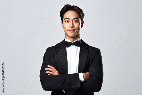 Portrait of asian handsome yong waiter in tuxedo and gloves while happily looking in camera with arms folded on white background.