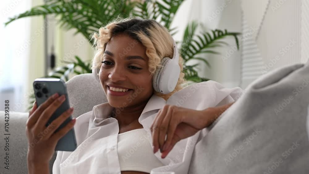 Smiling young black girl in headphones watching movie or film on streaming service on her smartphone Smiling young black girl in headphones watching movie or film on streaming service on her smartphone