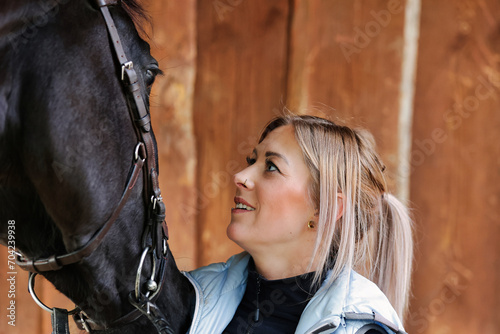 Girl blonde in blue quilted vest with ponytail plays with her horse, portraits of the woman with focus on her head close-up.