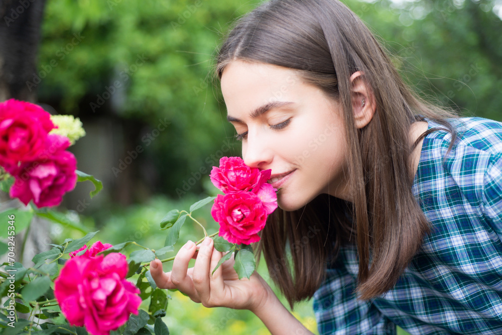 Naklejka premium Beautiful girl smelling a rose flower in spring park. Young woman in flowering garden with roses. Beauty model with spring flowers. Happy spring. Pretty woman enjoying smell flowers in spring park.