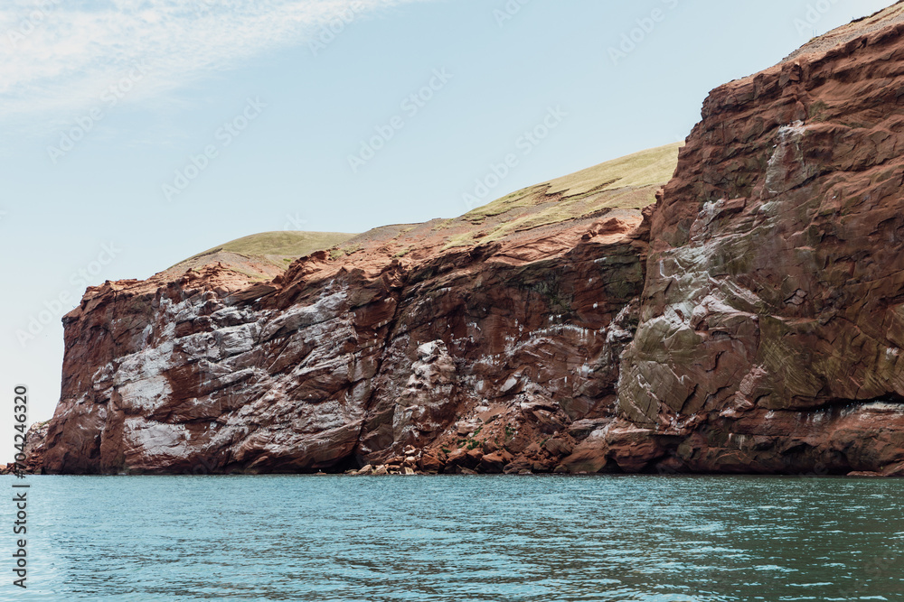vue sur une falaise en roche rouge avec des fientes d'oiseau en bord de mer avec du gazon sur le dessus en été lors d'une journée ensoleillée