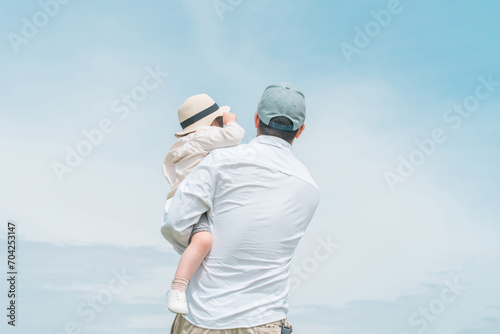 青空の見える公園で遊ぶパパと娘・親子の後ろ姿
