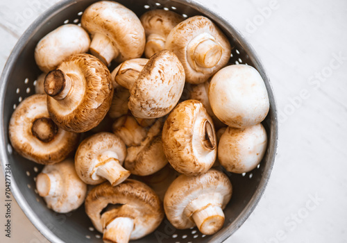 Raw mushrooms in an iron bowl on a white wooden background