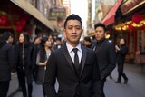 A young Asian man in a suit stands in a busy street with a blurred background