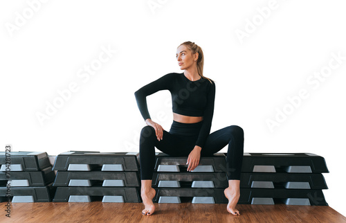 Purposeful young adult caucasian woman in black sportswear sitting on step platforms looks aside with pensive face expression against transparent background, relaxin after aerobics exercise photo