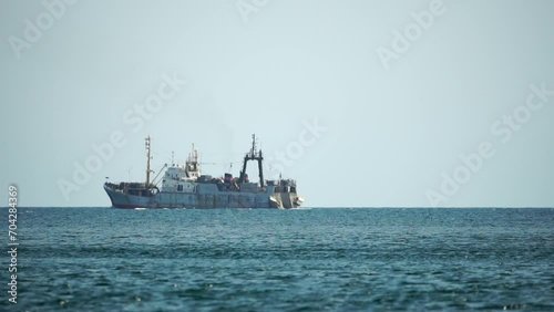 Fishing boat trawler catches fish while sailing on sea. A commercial fishing boat on the horizon in a distance sail to catch school of fish on calm sea surface in summer. Commercial catch of sea fish. photo