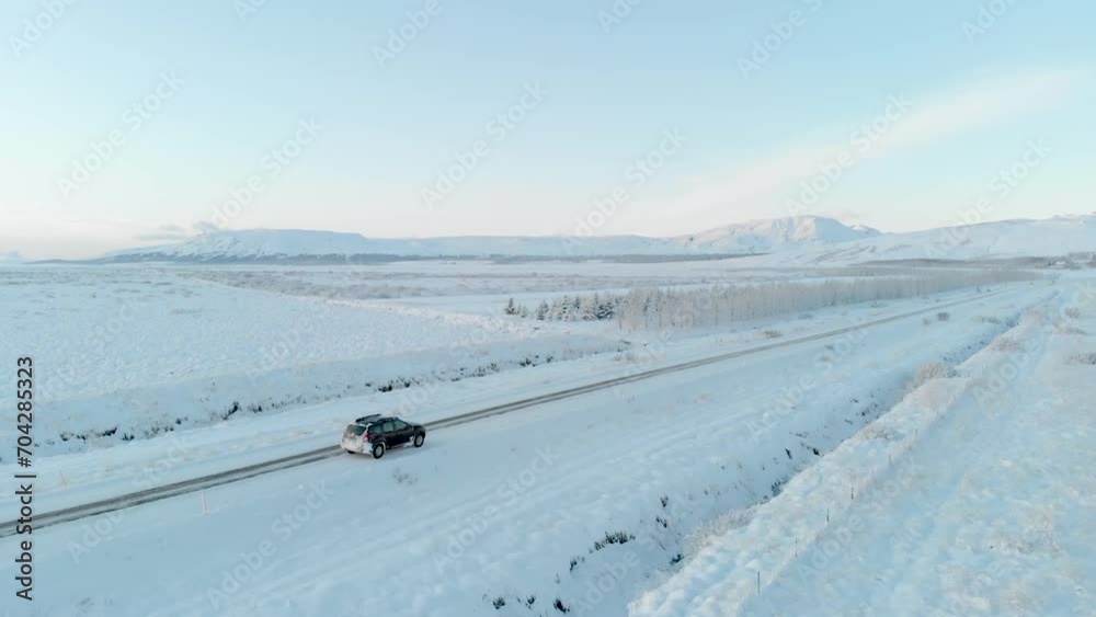 Drone shot panning around a driving car on vast empty snow covered landscape in Iceland Drone shot panning around a driving car on vast empty snow covered landscape in Iceland