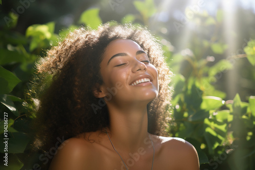 A woman joyfully touching her flawless, glowy skin with a serene expression, soft sunlight illuminating her face, and a lush green background