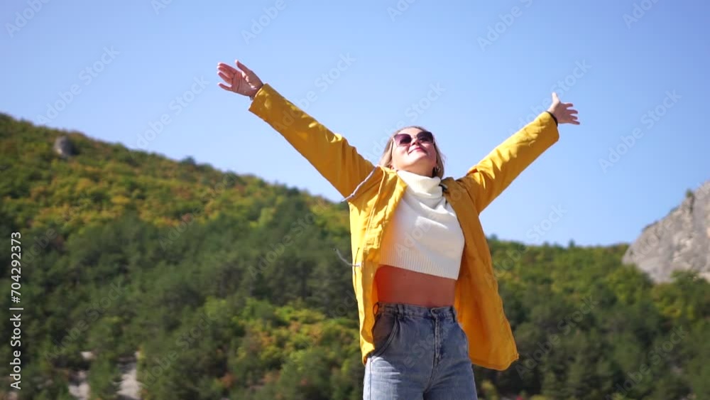 Cheerful happy woman tourist with carefree smile against backdrop of autumn mountains and serene lake. Concept of freedom and joy. Female hiker in yellow jacket, arms raised, enjoying warm sun outdoor Cheerful happy woman tourist with carefree smile against backdrop of autumn mountains and serene lake. Concept of freedom and joy. Female hiker in yellow jacket, arms raised, enjoying warm sun outdoor