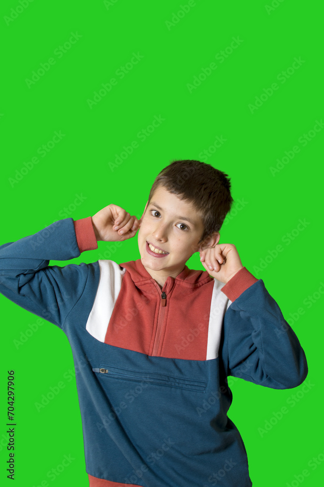 Portrait of a young boy looking front with hands on ears on green background Portrait of a young boy looking front with hands on ears on green background
