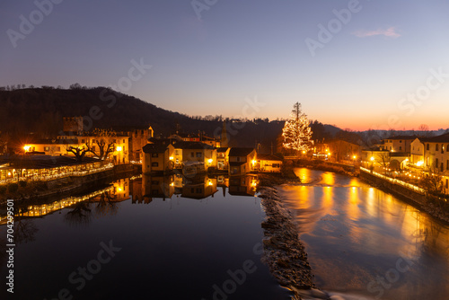 Borghetto sul Mincio, Christmas 2023: A magical nocturnal scene with historic houses reflected in the calm river, illuminated by a grand Christmas tree, evoking festive wonder in a tranquil village 