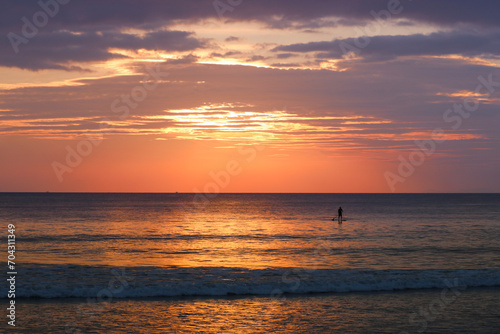Silhouette of a man on a SUP board in the sea against the backdrop of a colorful sunset. Tropical island, vacation, active recreation at sea, travel.