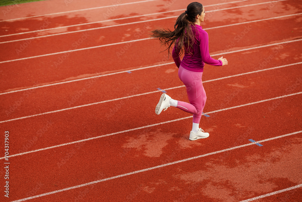 Rear view of a fit sportswoman running on running track on stadium.
