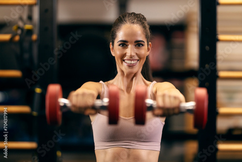 Portrait of a happy sportswoman exercising with dumbbells in a gym. © dusanpetkovic1