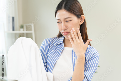 Asian young housewife woman having bad smelling clothes hand holding breath nose with finger, sniff smelly dirty stinky musty, look disgusting from clothes after washed, laundry out of machine at home