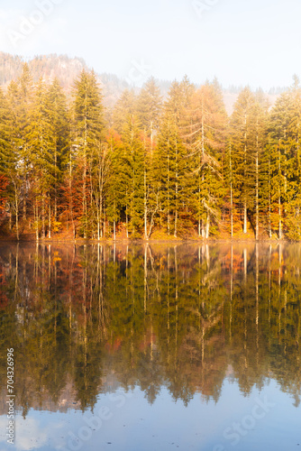 Autumn in Jezersko, Slovenia. Colourful trees reflecting in calm water surface. Bright and vibrant landscape scene. Nature background. Autumn walk.